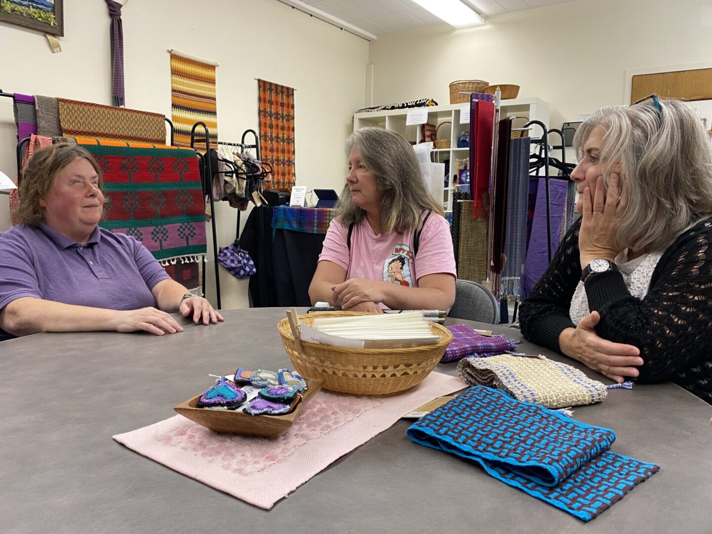 Sandra inquires about the program with two employees in front of a table with weaving samples