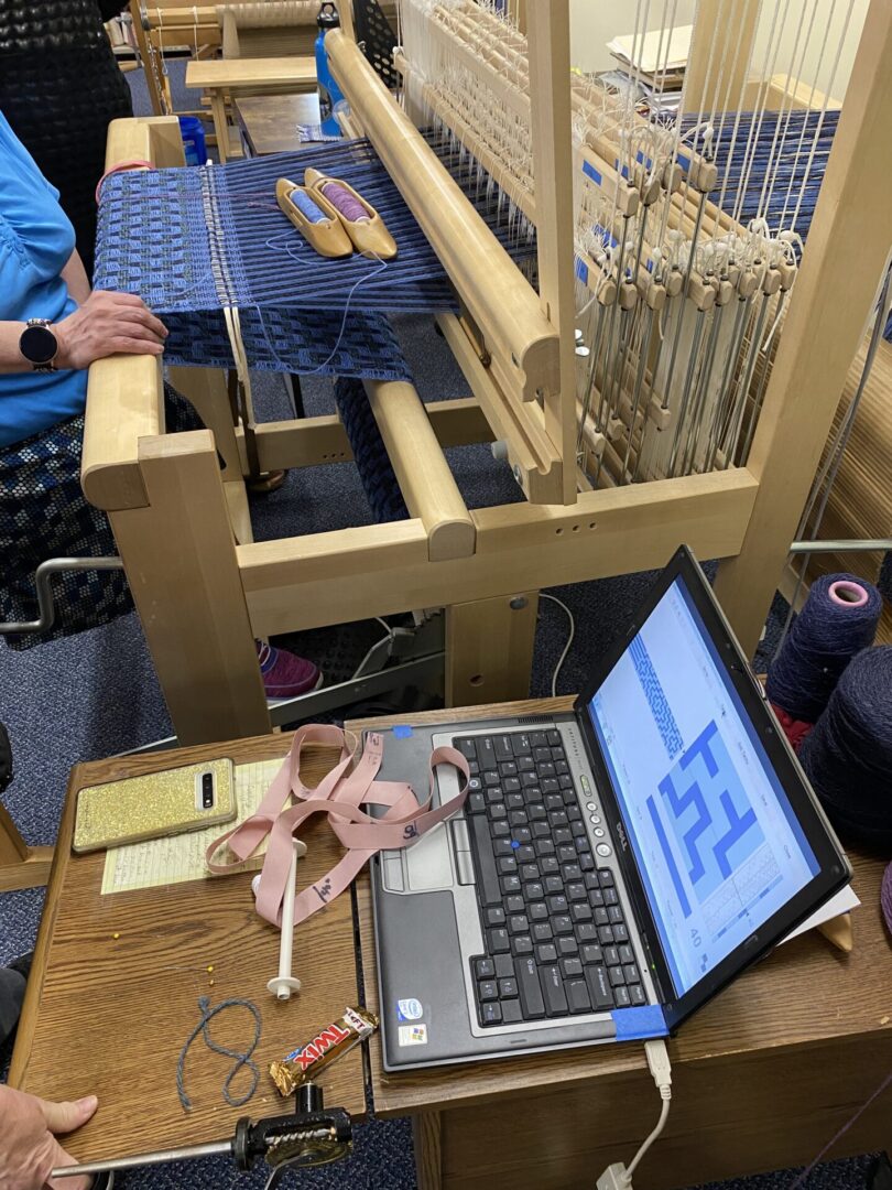 The loom presents an unexpected contrast to the modern laptop beside it.