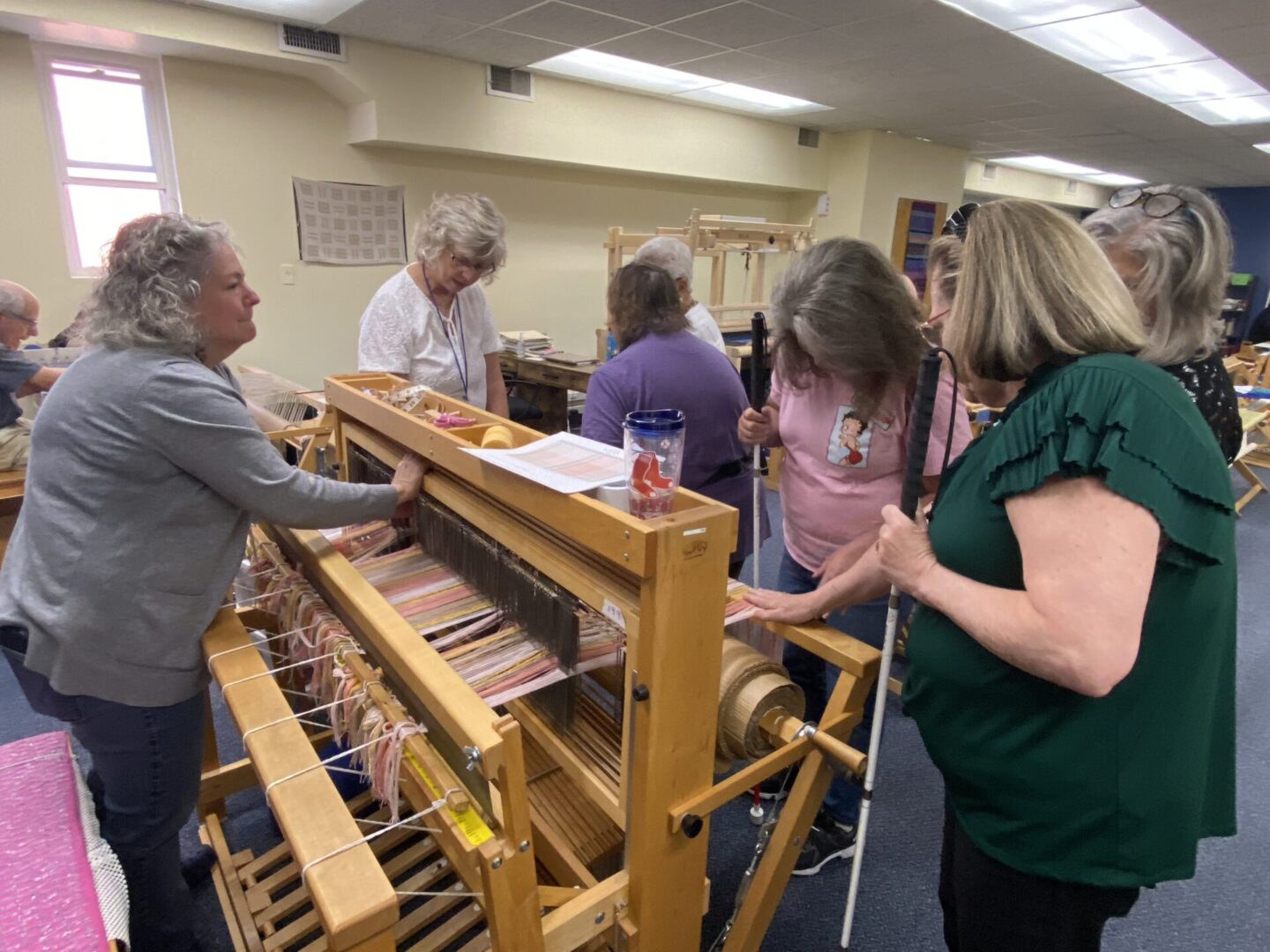 A group gathers to observe the progress on a weaver's loom.