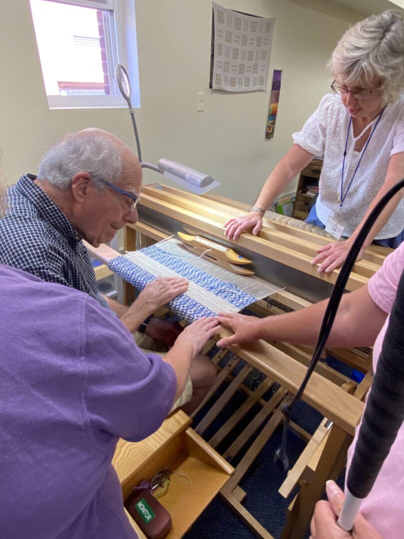 Everyone gathers around a weaver to feel the fine cloth on his loom.